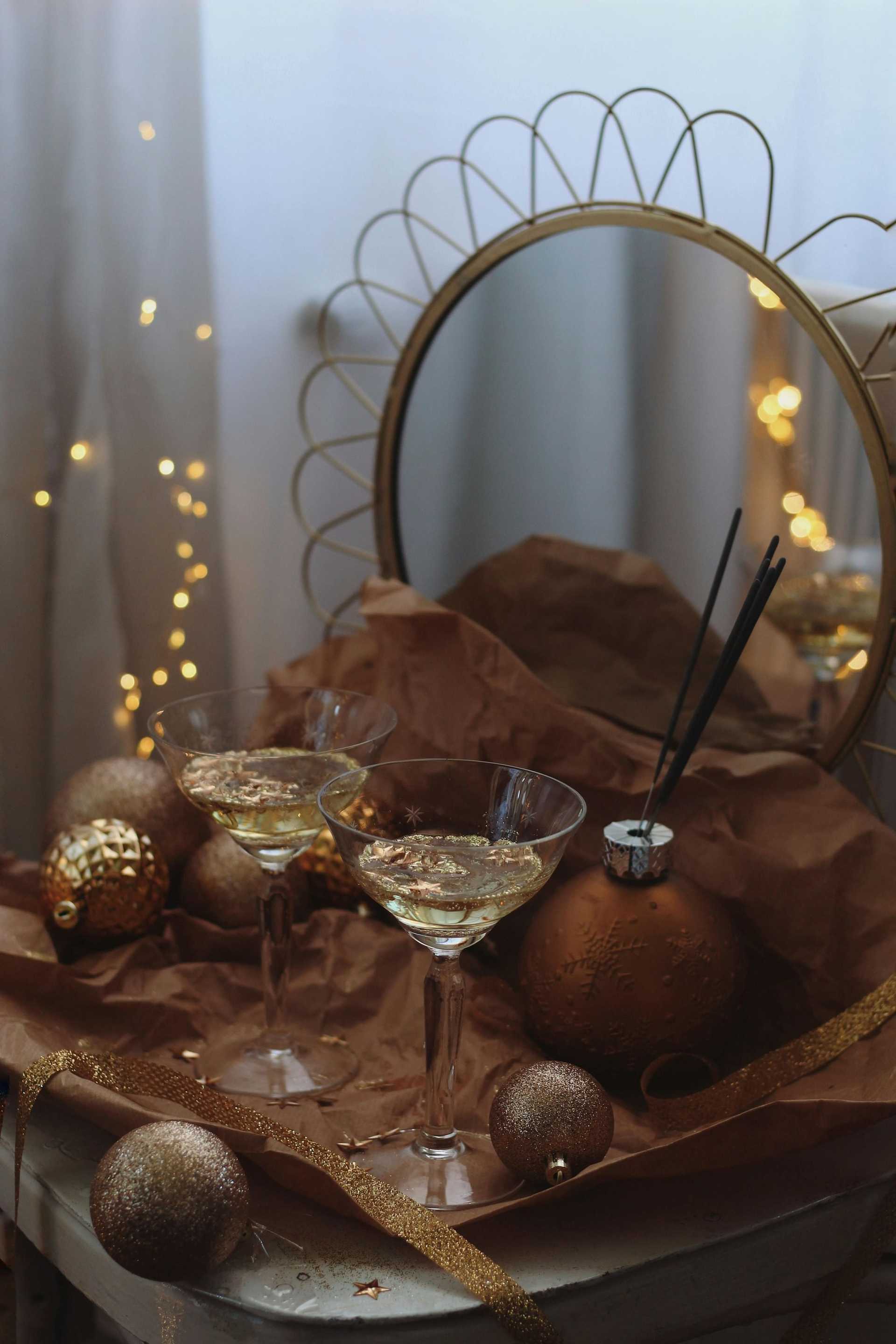 Two champagne glasses and gold decorations on a table with a round mirror in the background.